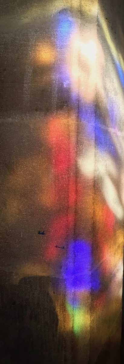 Sunlight shines through stained glass onto stone wall